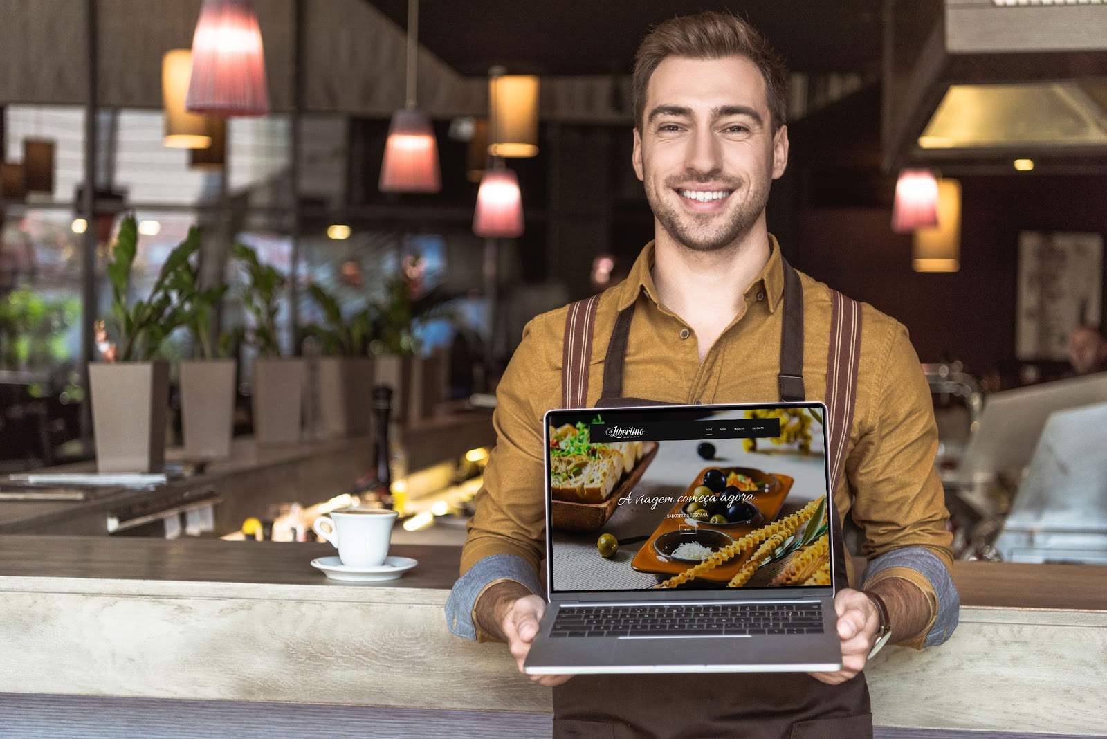 Homem num restaurante com um computador nas mãos, para mostrar o website de um restaurante